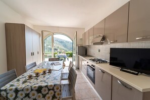 Une cuisine moderne dotée d’un grand téléviseur, d’une table à manger avec des chaises et offrant une vue sur l’extérieur.