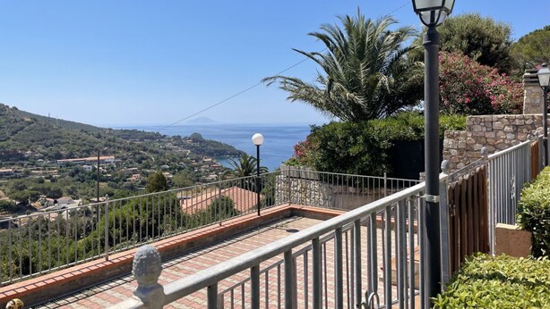 A balcony with a clear view of a coastal landscape, a stone wall, and a street lamp.