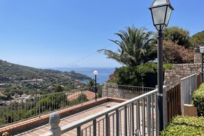 Ein Balkon mit freiem Blick auf eine Küstenlandschaft, eine Steinmauer und eine Straßenlaterne.