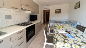 A compact kitchen with a stove, oven, and cabinets, a dining area with a table and chairs, and a bed with a floral bedspread.