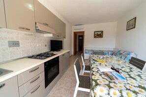 Une cuisine compacte équipée d’une cuisinière, d’un four et de placards, un coin repas avec une table et des chaises, et un lit recouvert d’une couvre-lit à motifs floraux.