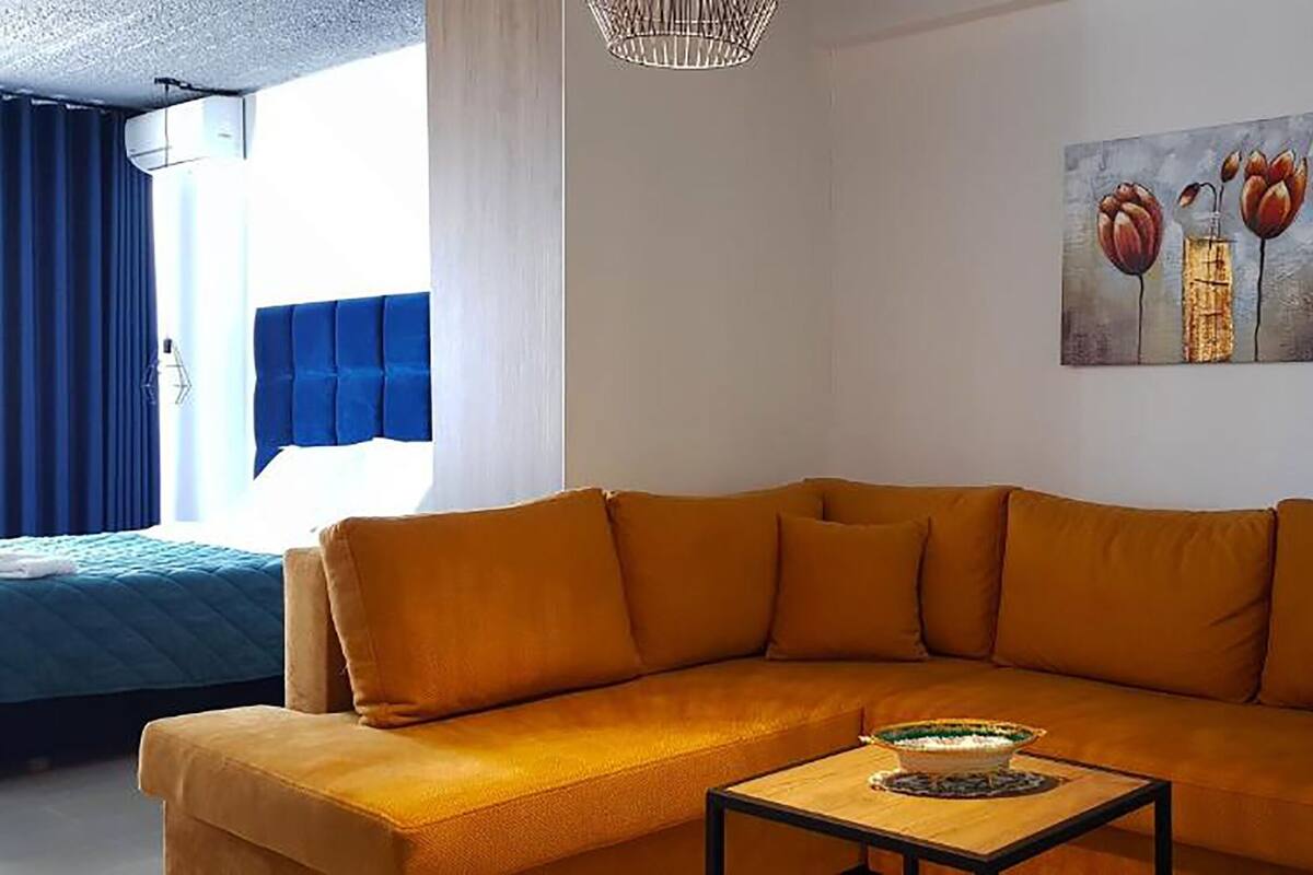 Un saló modern amb un sofà de color mostassa, una taula baixa de fusta i un quadre de flors a la paret.