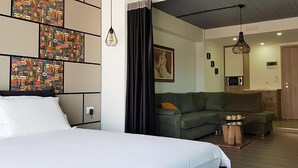 Ein modernes Hotelzimmer mit einem großen Bett, einem grünen Sofa, einem kleinen Tisch mit Snacks und einer Küchenzeile.