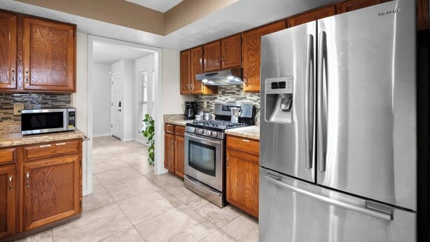 A modern kitchen with wooden cabinets, stainless steel appliances, and a skylight. - This spacious home has all you need with 2 primary suites, 2 guest bedrooms, and 3 bathrooms. There is no shortage of living space with a living room, 2 dining rooms, open floor plan w/fully-stocked kitchen, and onsite laundry. (El Paso)