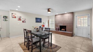 A dining area with a glass table, dark chairs, a patterned rug, a fireplace, and a door with a window. - This spacious home has all you need with 2 primary suites, 2 guest bedrooms, and 3 bathrooms. There is no shortage of living space with a living room, 2 dining rooms, open floor plan w/fully-stocked kitchen, and onsite laundry. (El Paso)