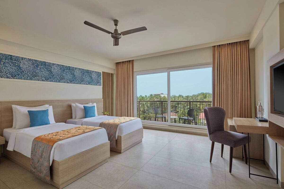 A hotel room with two beds, a desk, a chair, a television, and a balcony with a view.