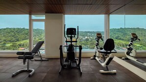 Et fitnesscenter med forskellig træningsudstyr, store vinduer og udsigt over et grønt landskab.