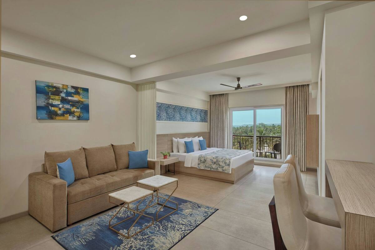 A modern hotel room with a sofa, a bed, a desk, and a balcony with a view.