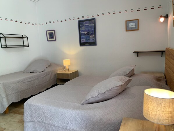 Une chambre avec deux lits simples, une table de chevet avec une lampe, un tableau encadré et une étagère.