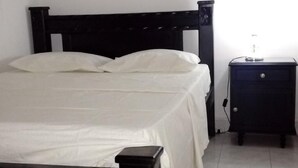A bed with white linens, a black headboard, and a small bedside table with a lamp. - Room in House - Taminaka Hostel en Santa Marta - Shared Room 2 (Santa Marta)