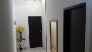 A hallway with a ceiling fan, a black door, a mirror, and a small table with a vase of yellow flowers. - Room in House - Taminaka Hostel en Santa Marta - Shared Room 2 (Santa Marta)