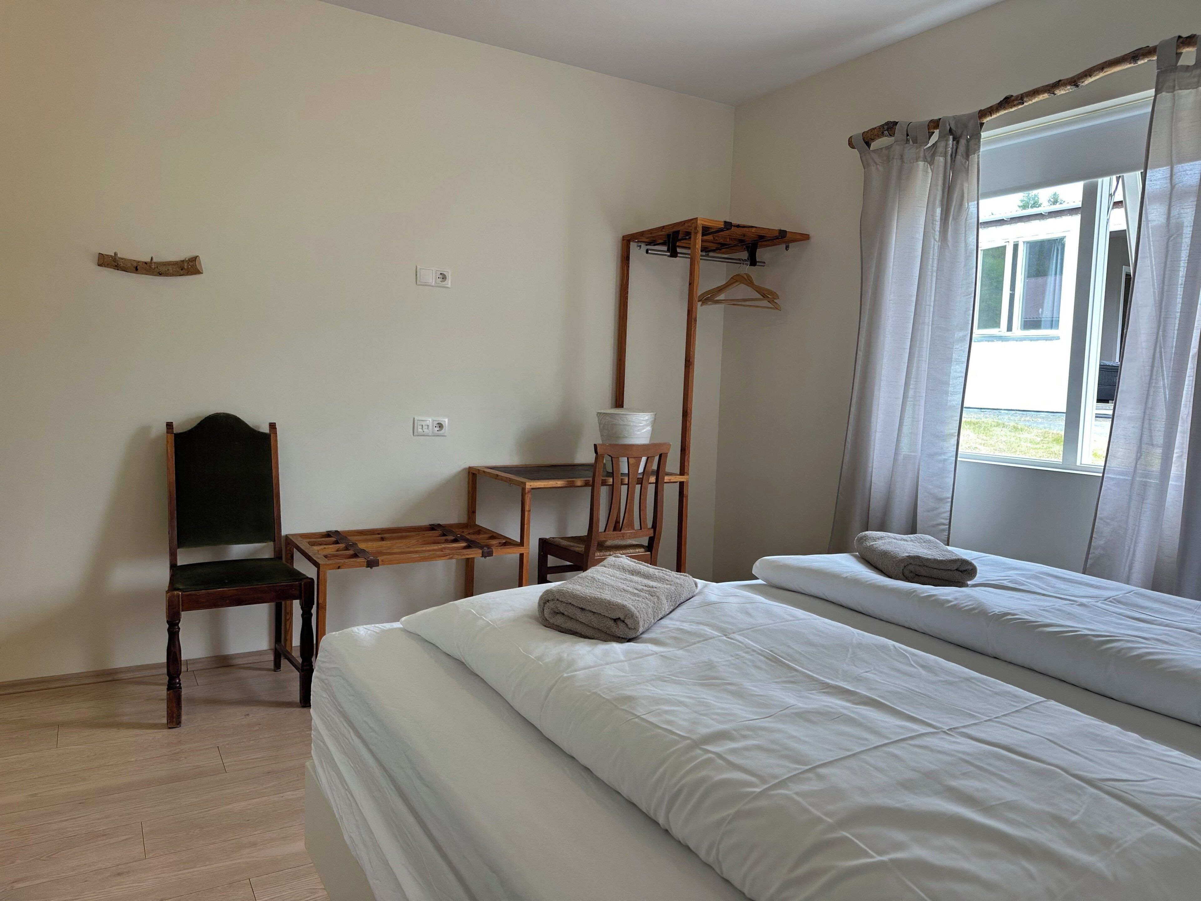 Un dormitorio con cama, una silla, una mesita y una ventana con cortinas.