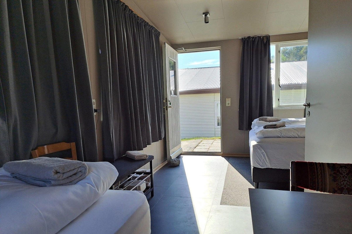 A hotel room with two beds, a desk, and a view of the outside.
