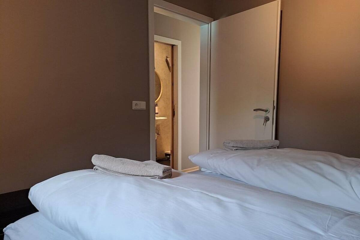 Habitación de hotel con dos camas, baño visible a través de una puerta abierta y un espejo en la pared.