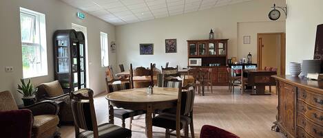 A spacious dining area with a round table and chairs, a kitchen with a microwave and stove, and a clock on the wall.