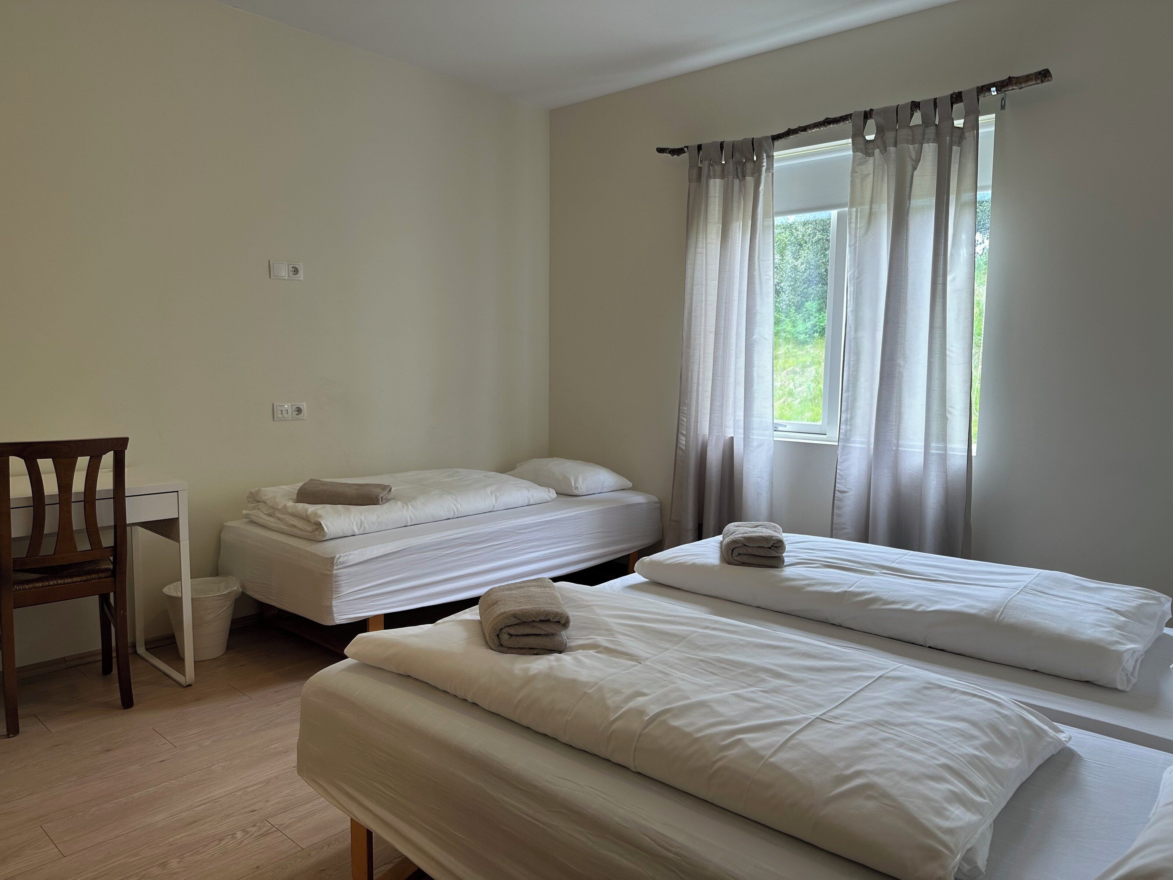 Un dormitorio con dos camas, una silla y una ventana con cortinas.