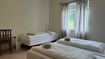 Un dormitorio con dos camas, una silla y una ventana con cortinas.