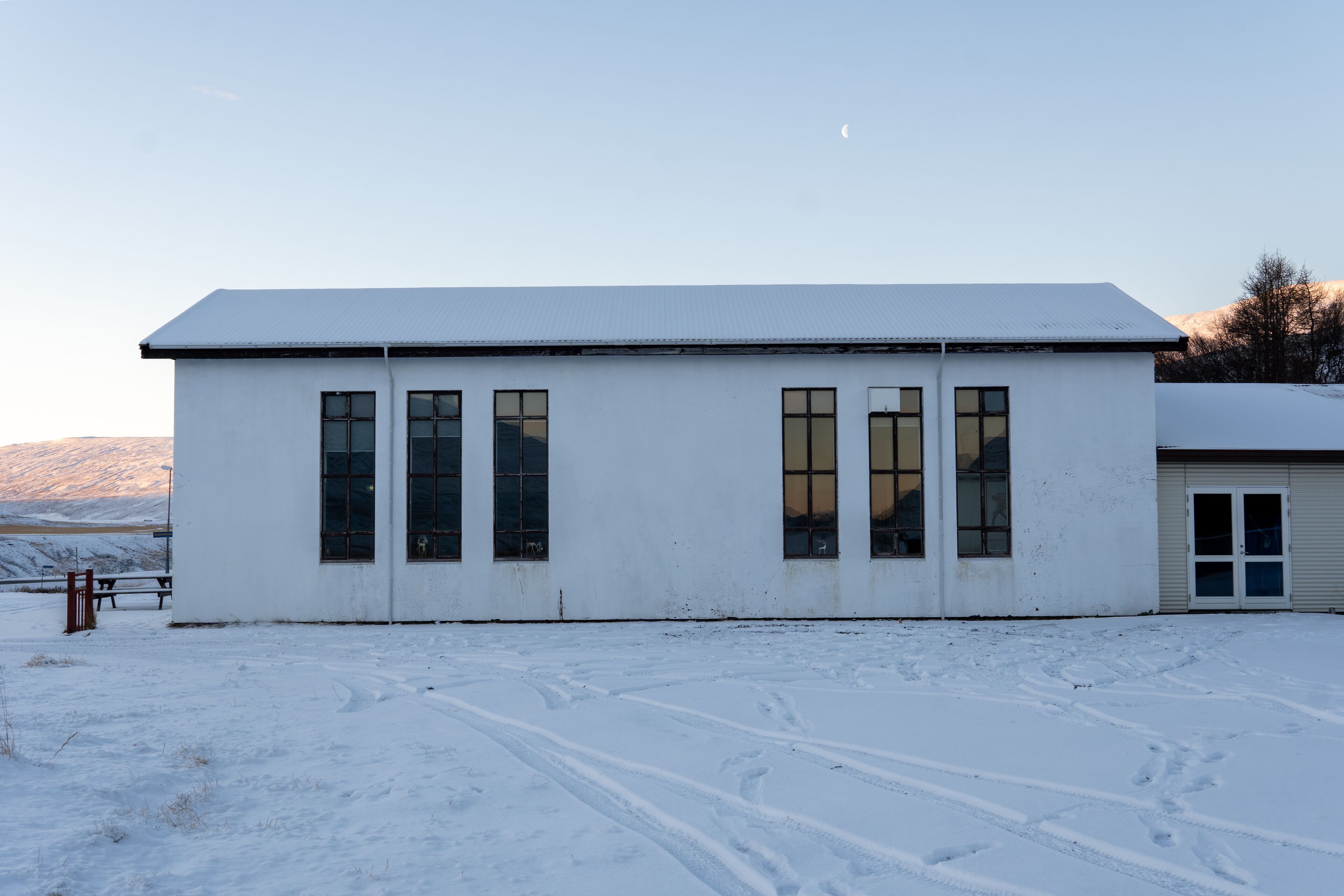 A white building with large windows and a flat roof, situated in a snowy landscape with a clear sky.