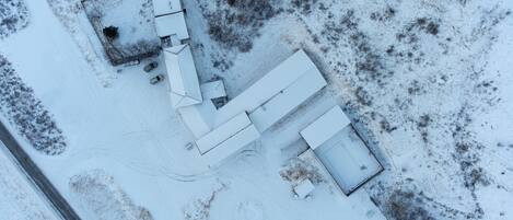 An aerial view of a snow-covered property with a large building, several smaller structures, and a paved driveway.