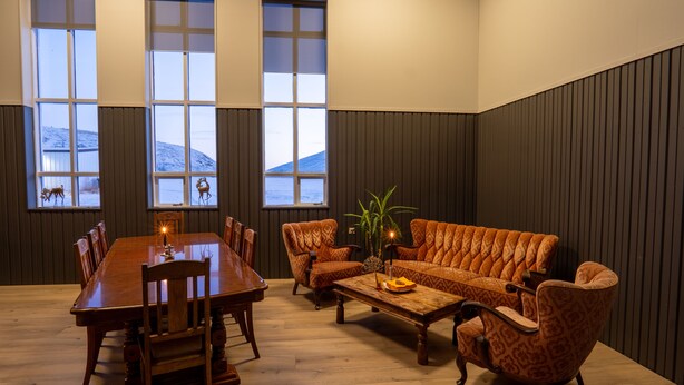A dining area with a wooden table and chairs, a patterned sofa, and a potted plant. - Hotel Studlagil  (Egilsstaðir)