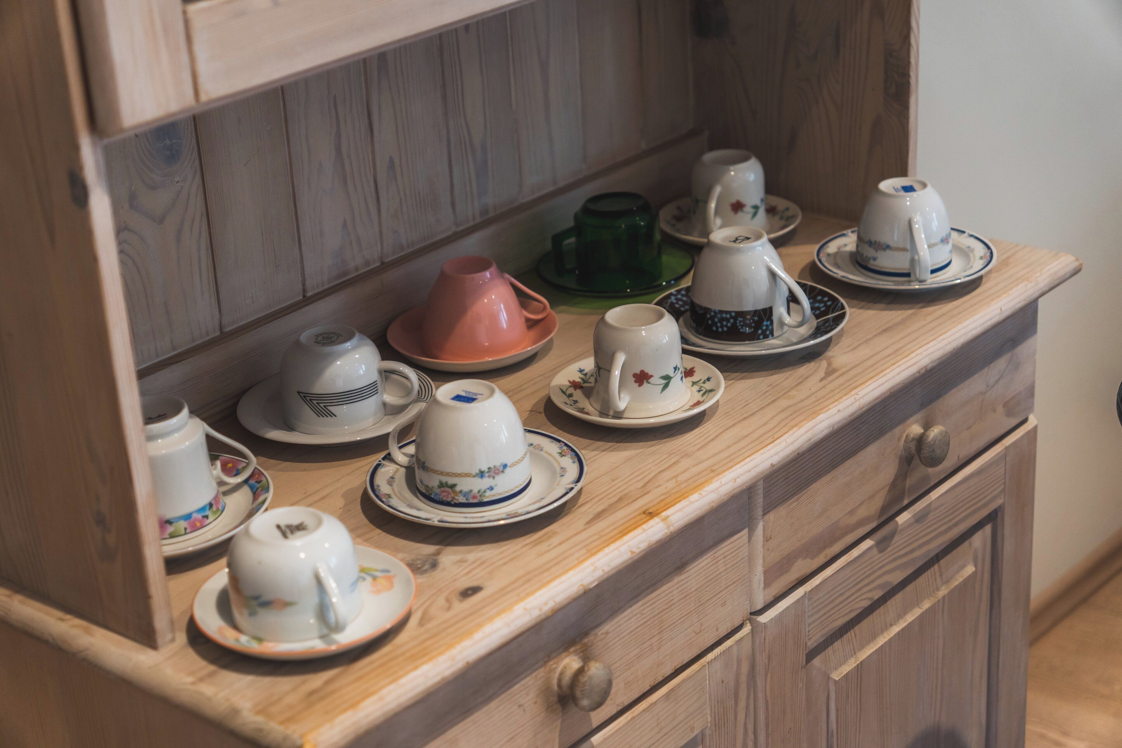 Un mueble de madera con varios juegos de té y tazas de cerámica.