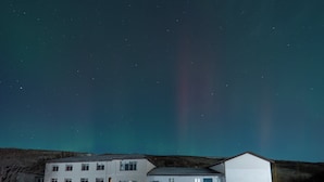 A building with multiple windows and a door, a covered area with a bench, and a snowy ground. - Hotel Studlagil  (Egilsstaðir)