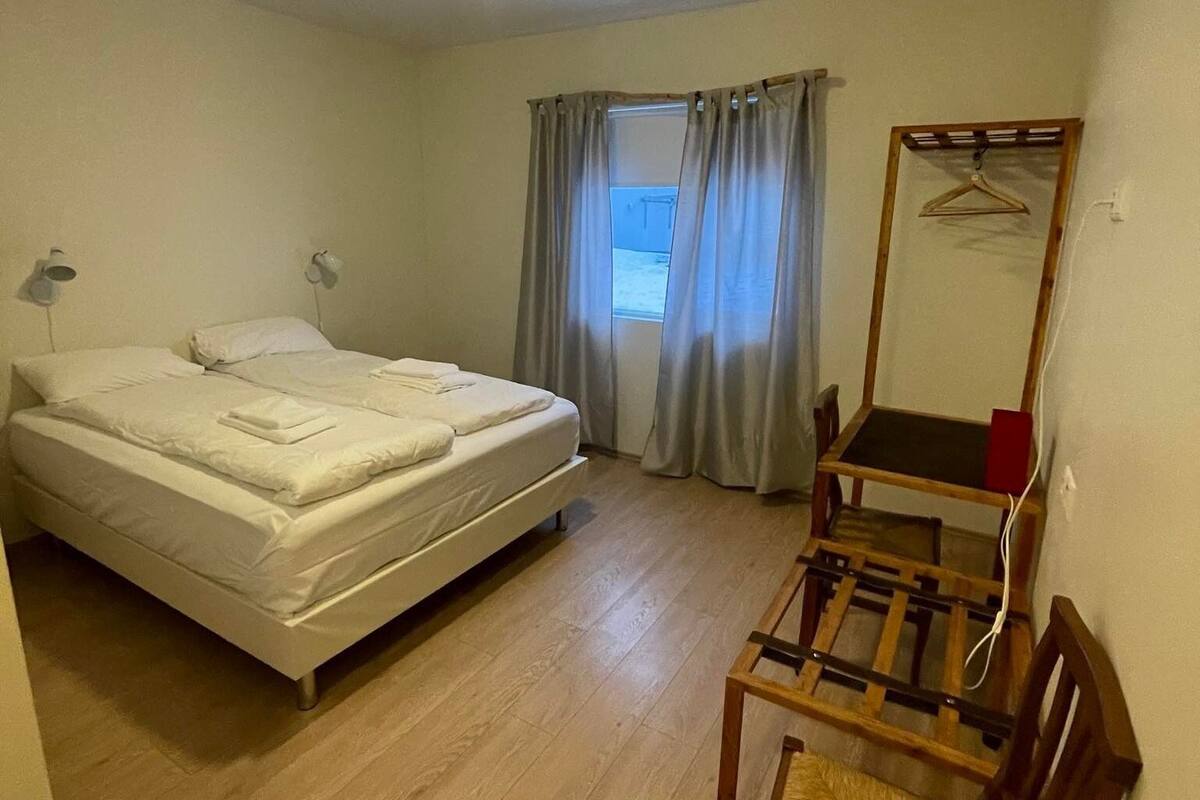 Un dormitorio con una cama doble, un escritorio con silla, un espejo y una ventana con cortinas.