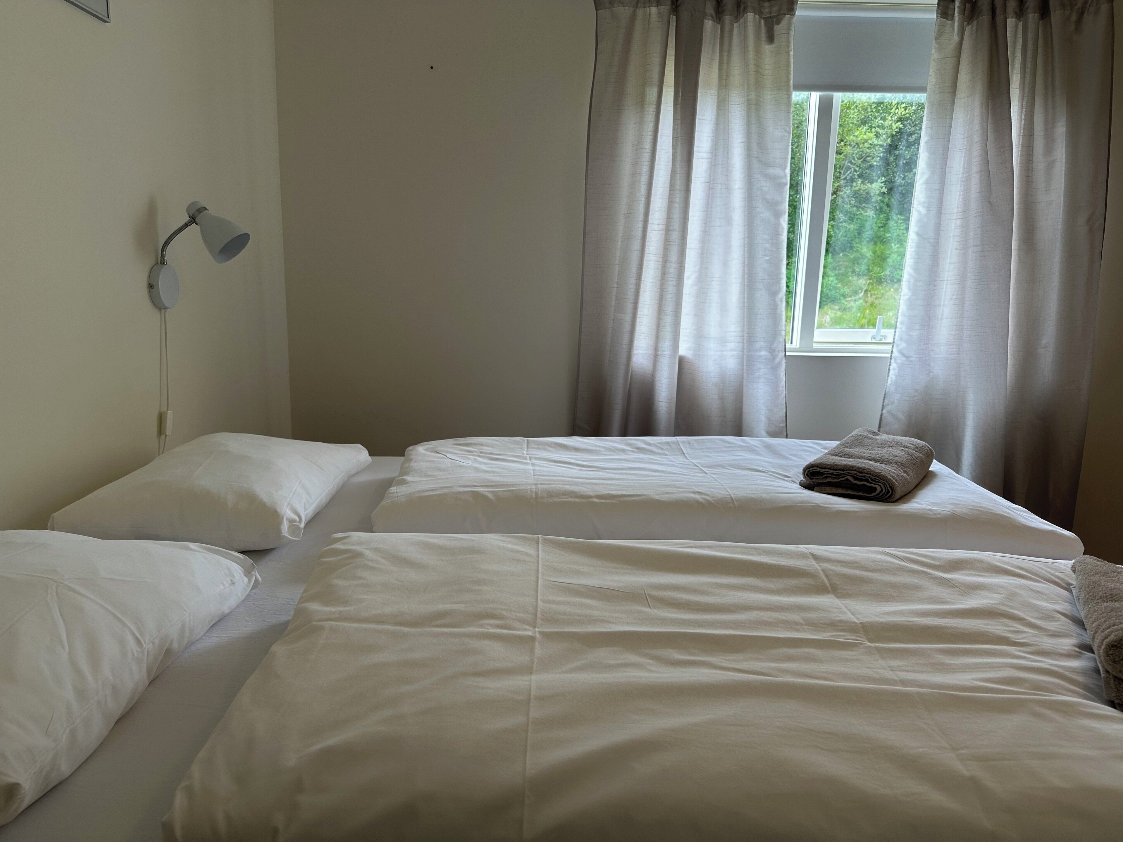 Une chambre d’hôtel avec deux lits, une lampe de chevet et une fenêtre avec des rideaux.
