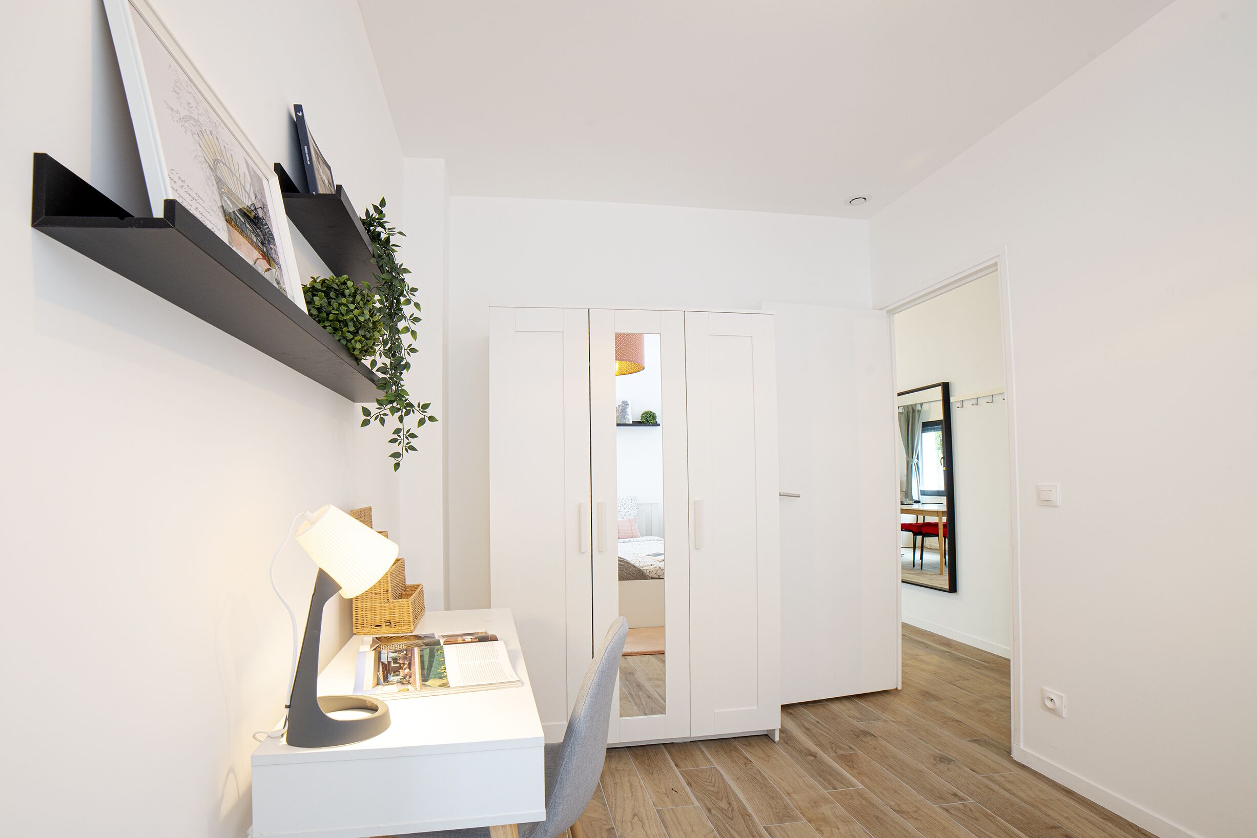 A modern, minimalist room with a white desk, a lamp, and a bookshelf.