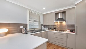 Una cucina moderna con mobili grigi, un piano di lavoro bianco, un forno integrato, un fornello, un lavello e una finestra con persiane.