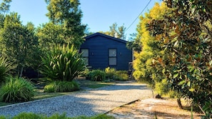 Une maison avec une allée en gravier, entourée de différentes plantes et arbres.