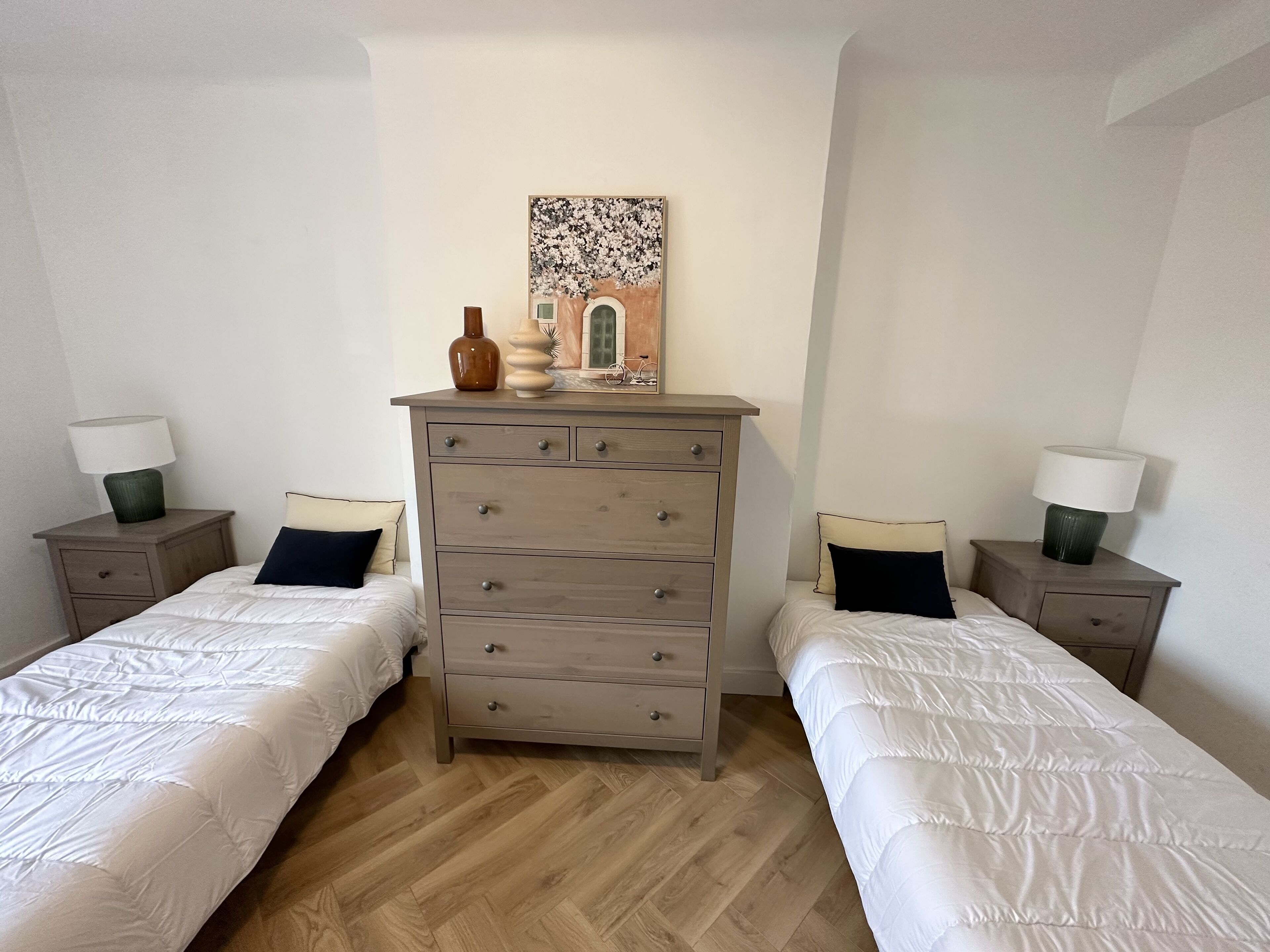 A bedroom with two beds, a dresser, and a painting on the wall.