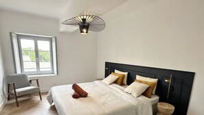 A bedroom with a bed, a chair, a window, and a unique ceiling light fixture.