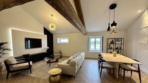 A spacious living area with a sofa, dining table, and a TV mounted on the wall.