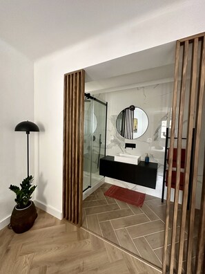 Une salle de bain moderne avec une douche à l’italienne en verre, un miroir rond et un meuble-lavabo noir.
