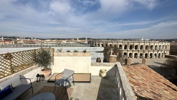 A rooftop terrace with a view of a historic building, a seating area with a table and chairs, and a potted plant.