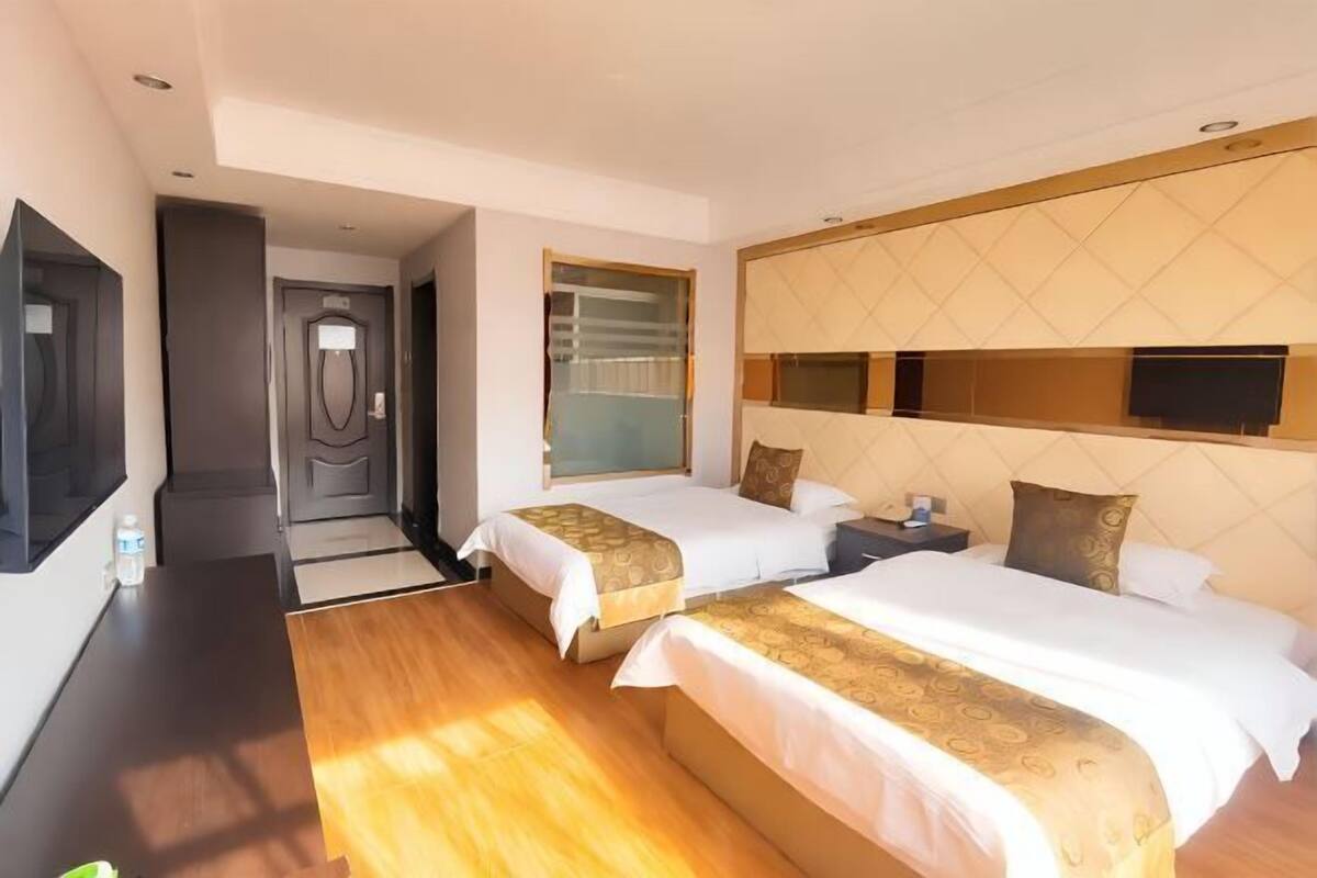 A hotel room with two beds, a TV, a minibar, and a bathroom.