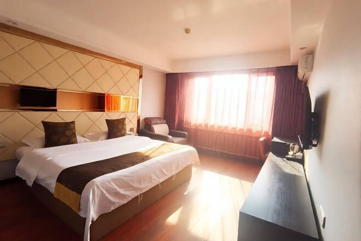 A hotel room with a large bed, a desk, a chair, a TV, and a window with curtains.