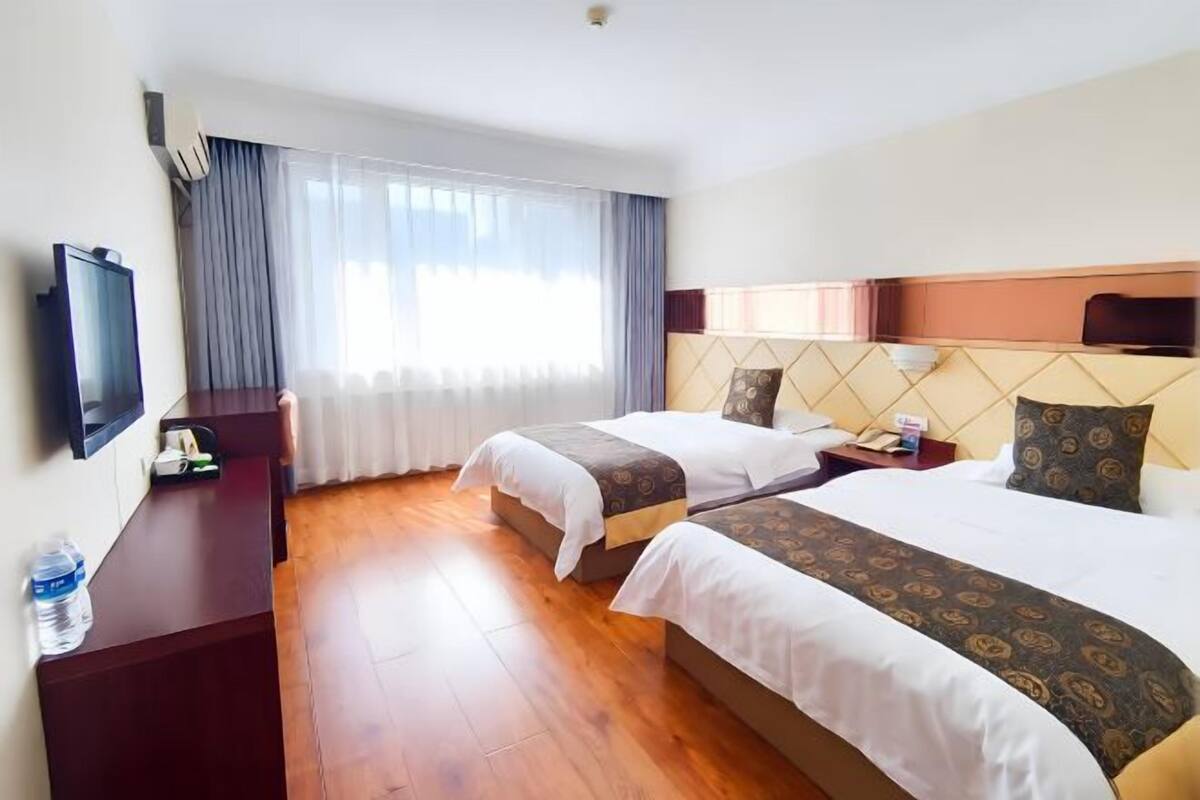 A hotel room with two beds, a desk, a TV, and a window with curtains.