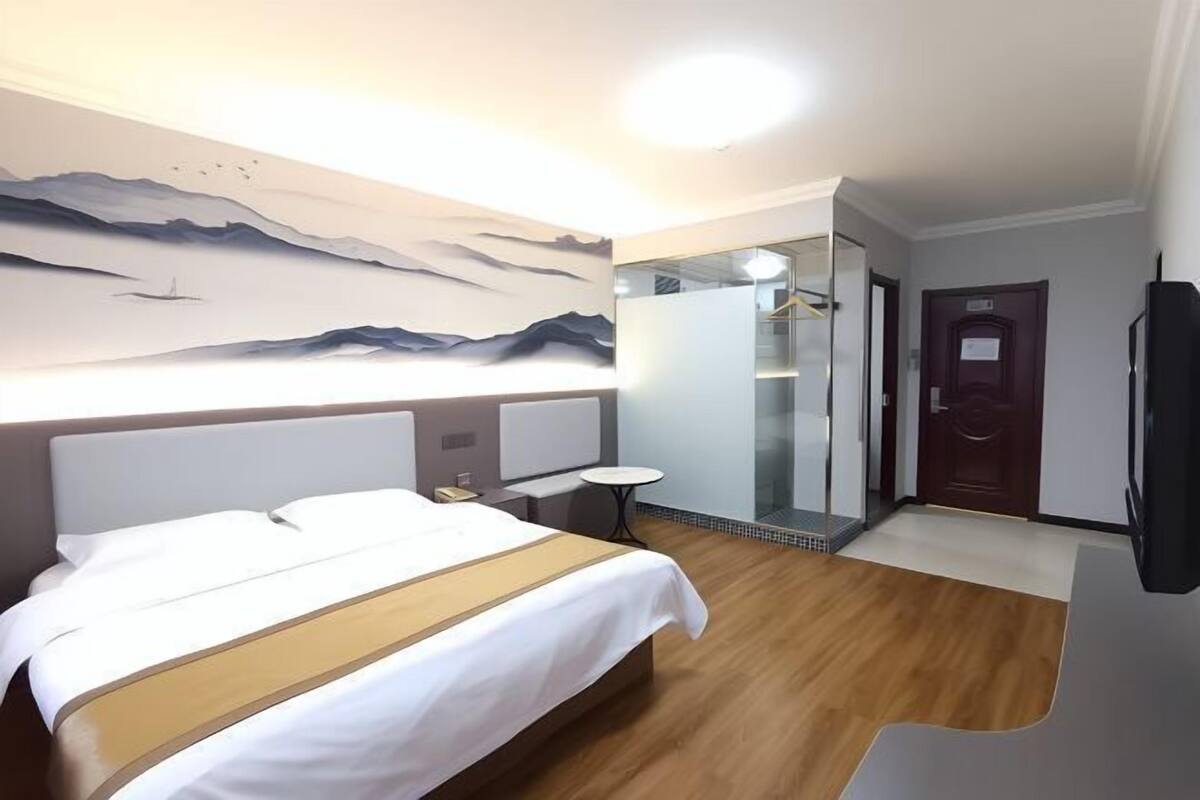 A hotel room with a bed, a mirror, a TV, and a shower area.