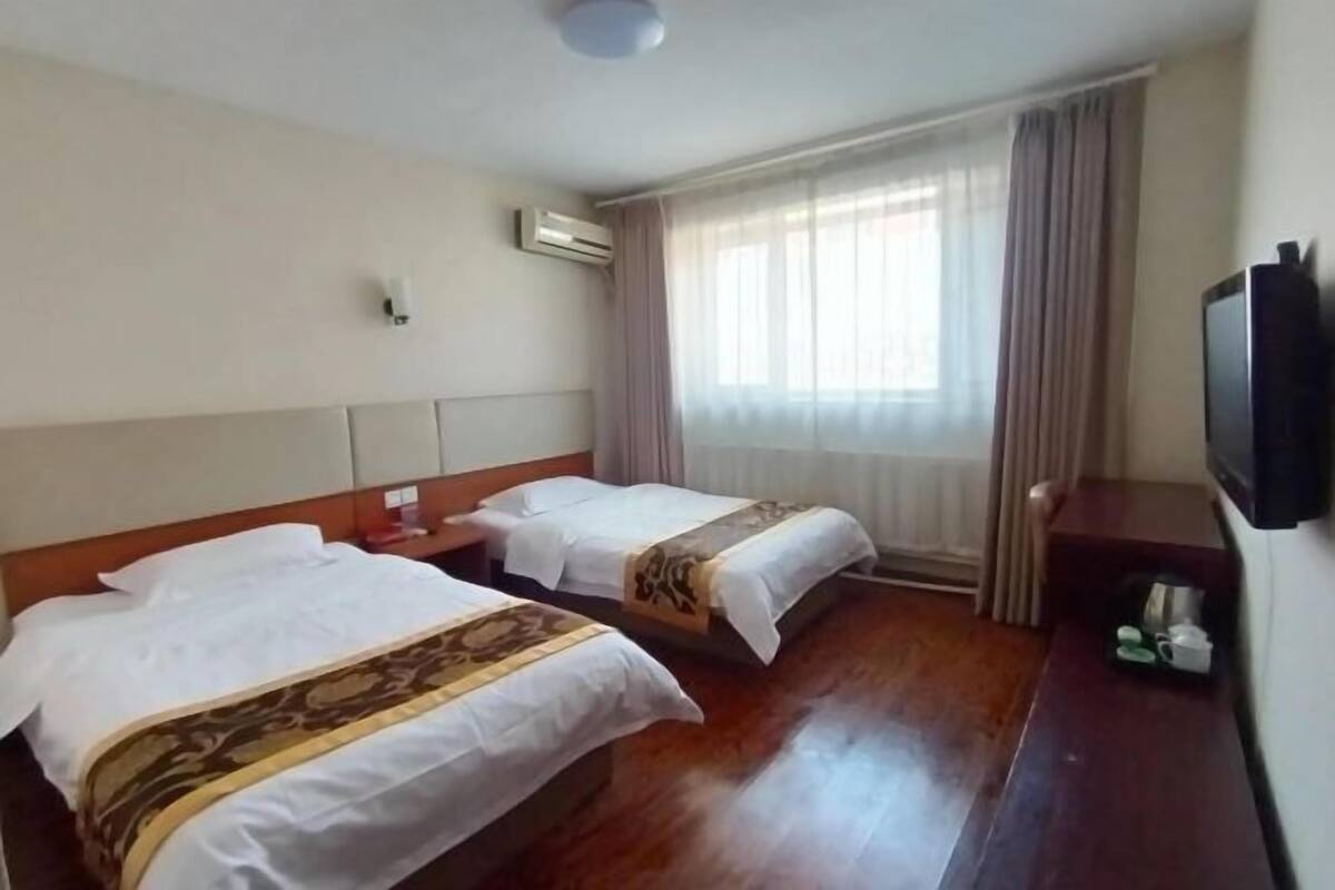 A hotel room with two beds, a flat-screen TV, a bedside table, and a window with curtains.
