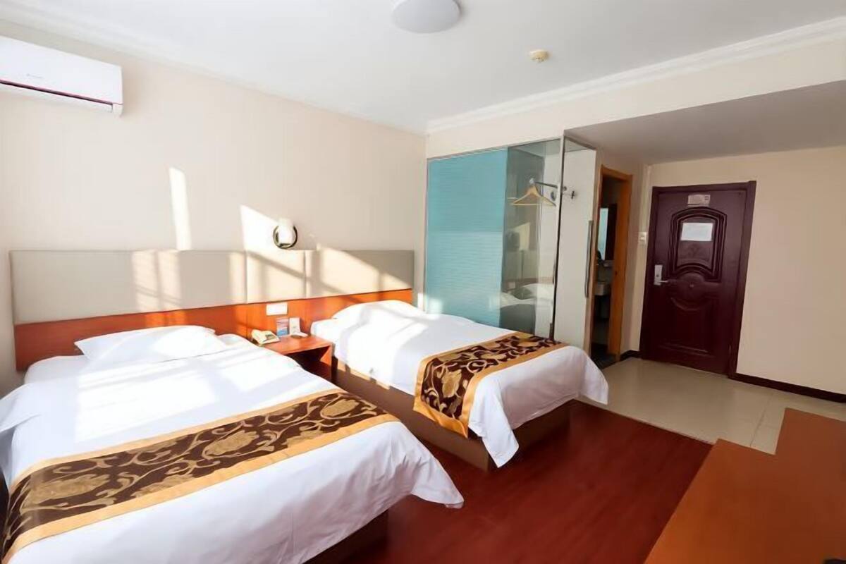 A hotel room with two beds, a wooden headboard, a glass shower enclosure, and a door with a handle.