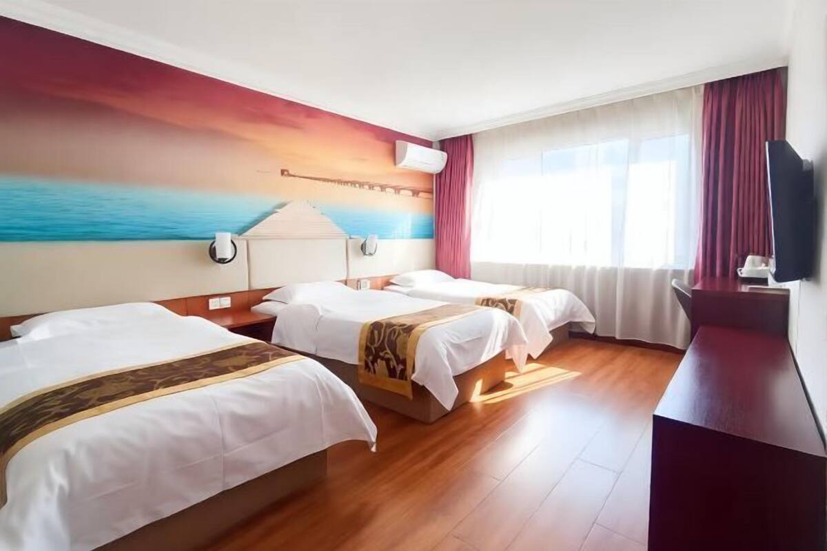 A hotel room with two beds, a desk, a TV, and a painting of a sunset over the ocean.