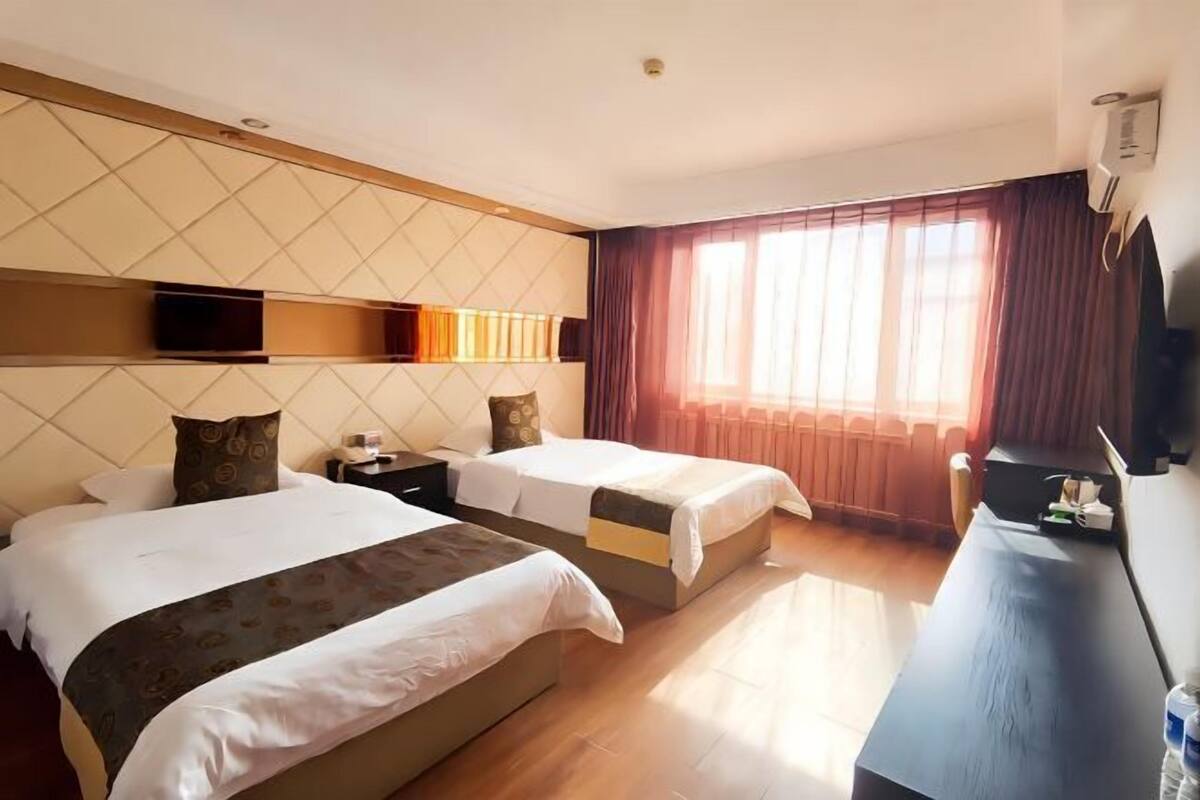 A hotel room with two beds, a desk, a TV, and a window with curtains.