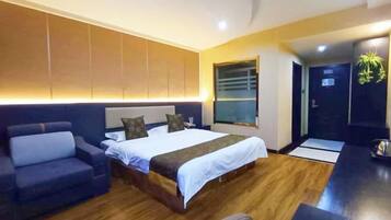 A modern hotel room with a large bed, a sofa, a desk, and a view of the outside.
