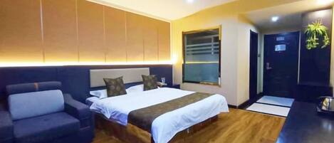 A modern hotel room with a large bed, a sofa, a desk, and a view of the outside.