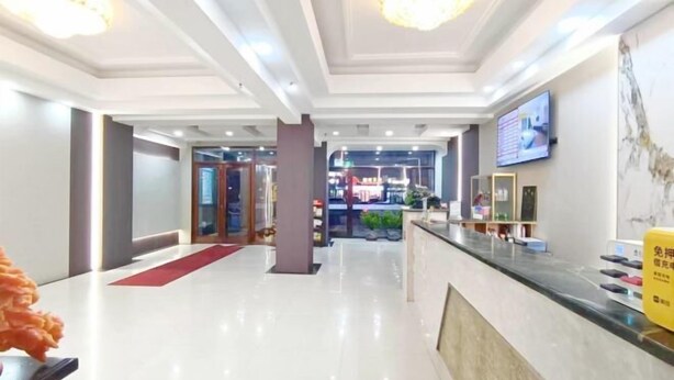 Un vestíbulo de hotel con mostrador de recepción, alfombra roja y una pantalla de televisión en la pared.