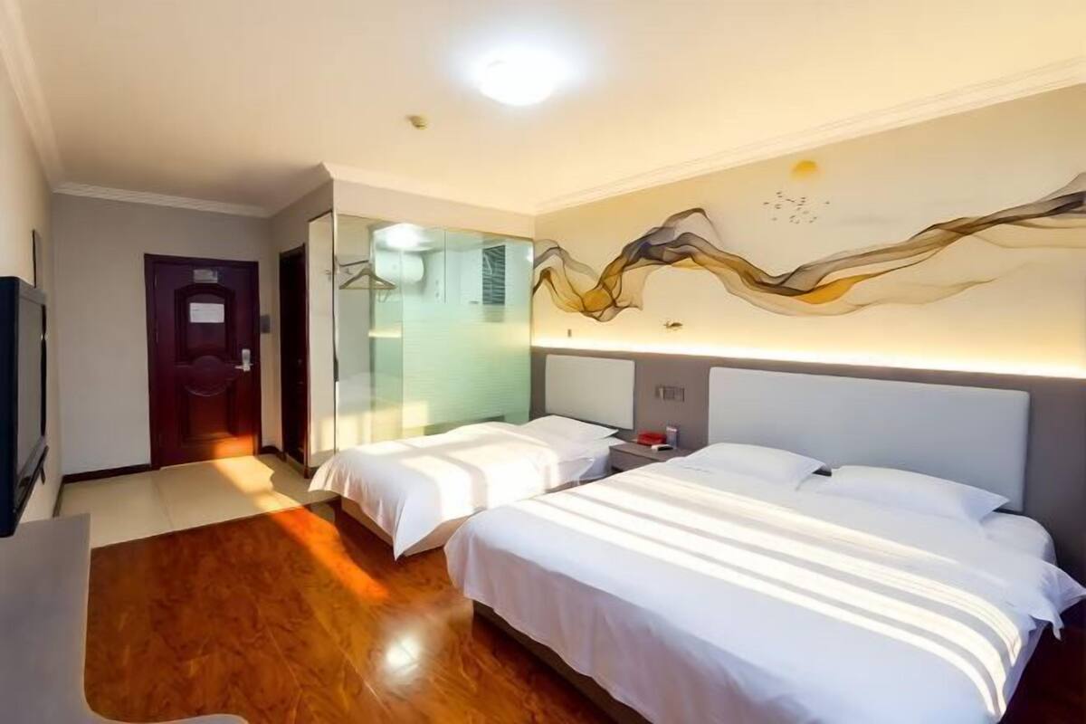 A hotel room with two beds, a wooden floor, a wall-mounted TV, and a unique abstract wall design.