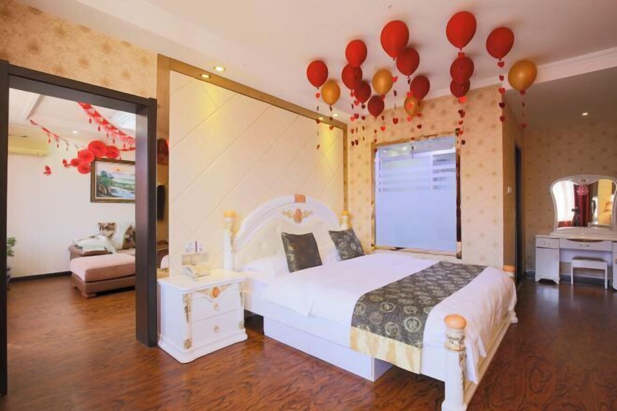 A bedroom with a large bed, a bedside table, a dresser, and a desk with a chair.