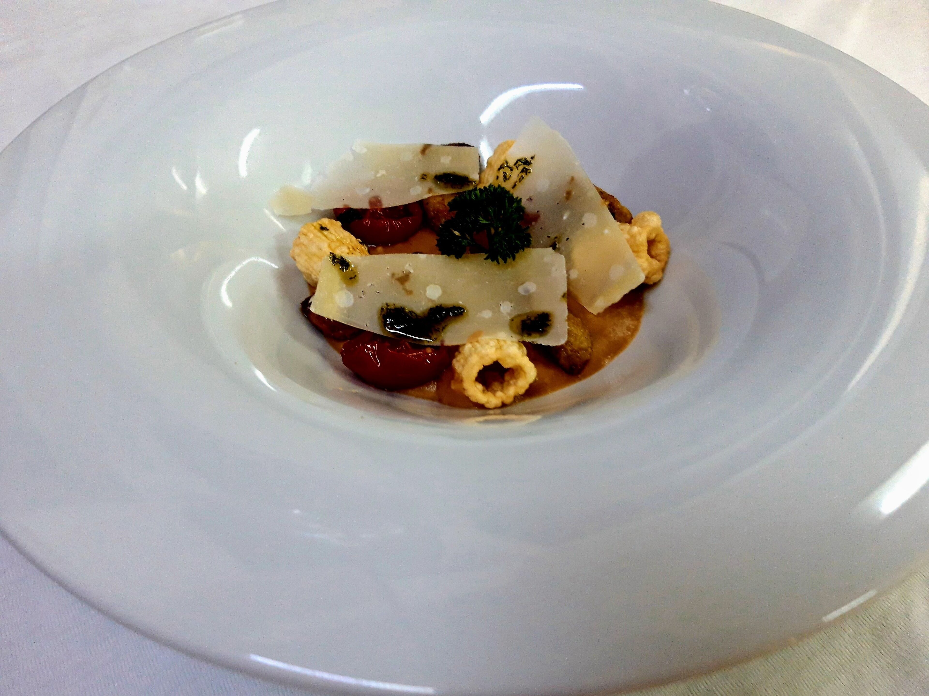 Un plato blanco con un guiso que contiene varios alimentos, incluyendo un trozo de pescado, verduras y posiblemente algunas guarniciones.